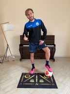 Un calciatore in posa con un pallone da calcio sul tappeto FootSkills, pronto per iniziare il suo allenamento tecnico in casa.