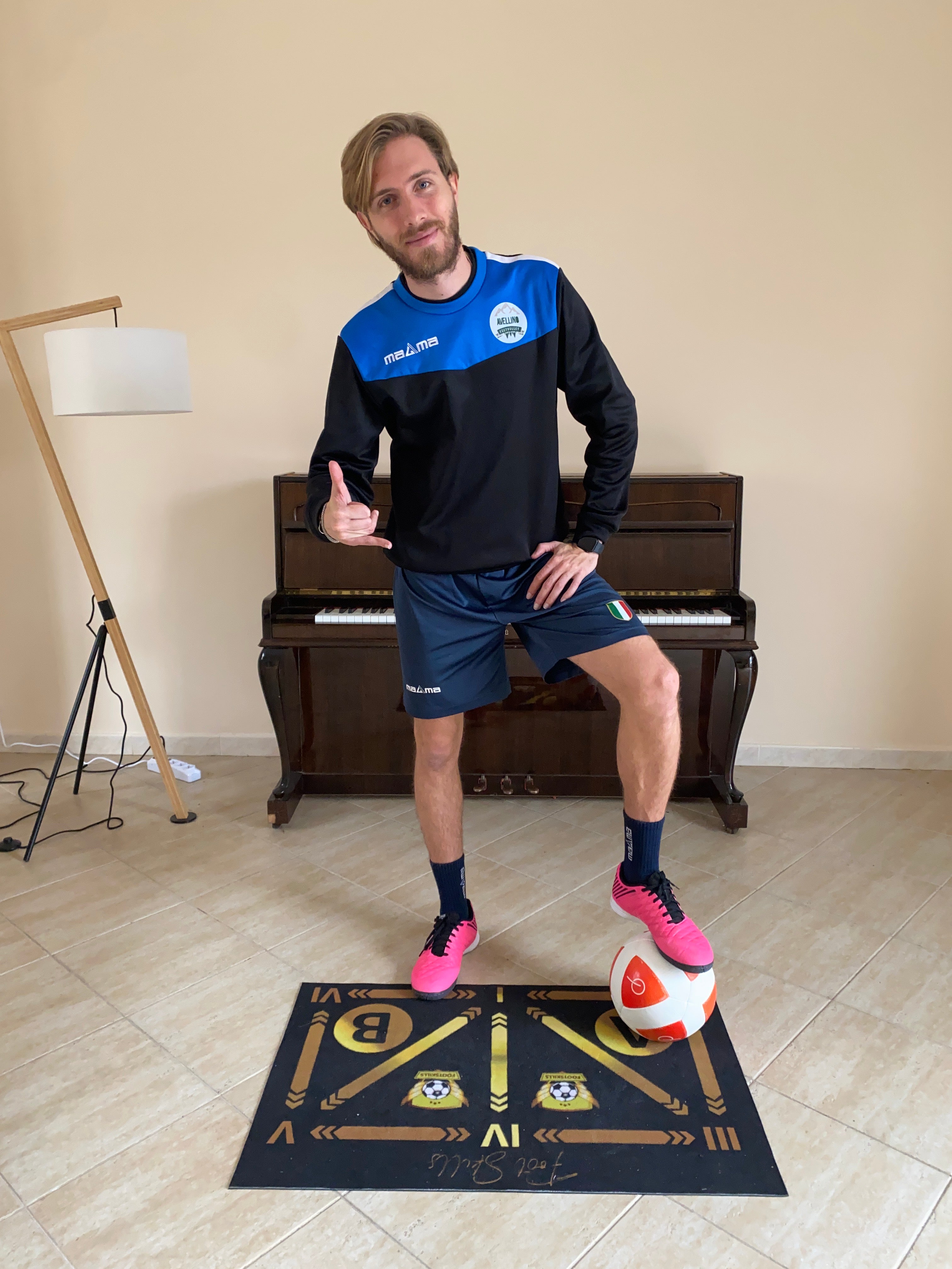 Un calciatore in posa con un pallone da calcio sul tappeto FootSkills, pronto per iniziare il suo allenamento tecnico in casa.