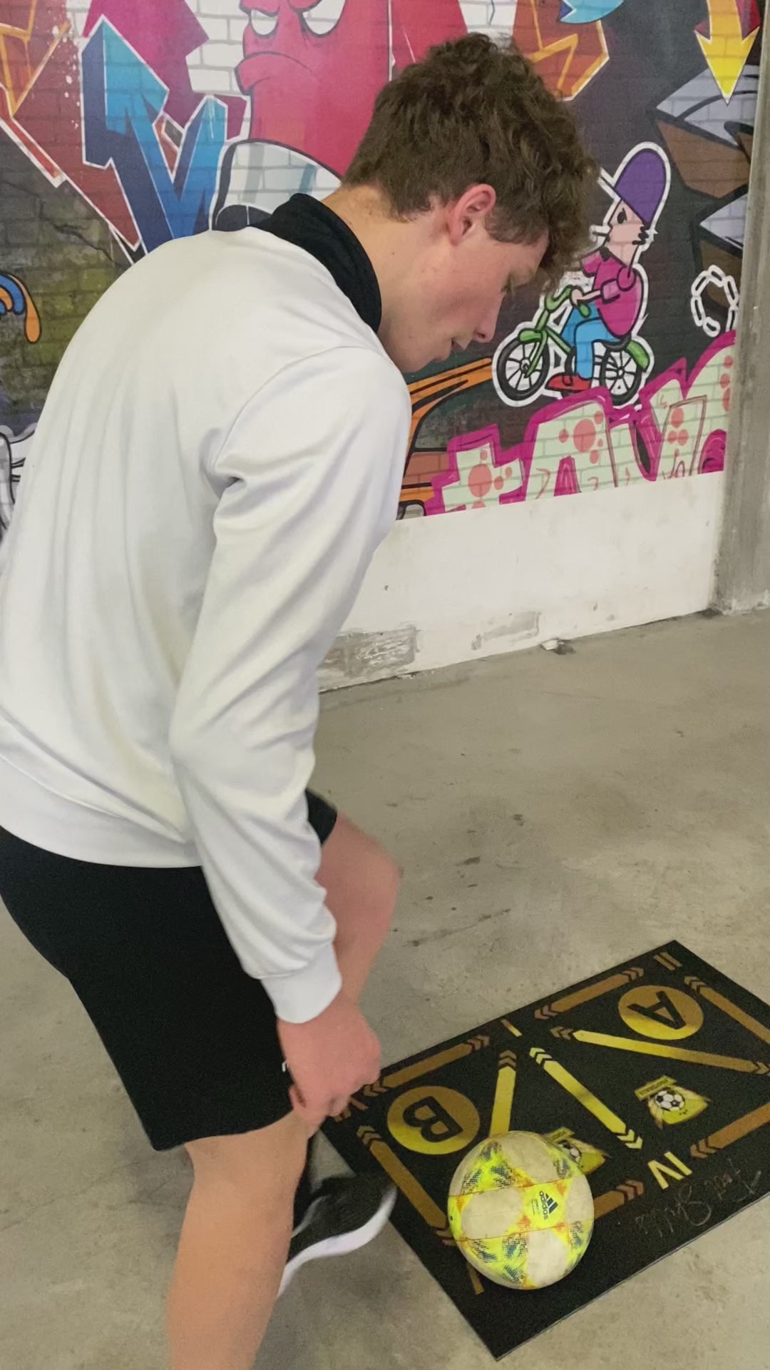 Soccer player performing advanced ball drills on a training mat in front of a graffiti wall.