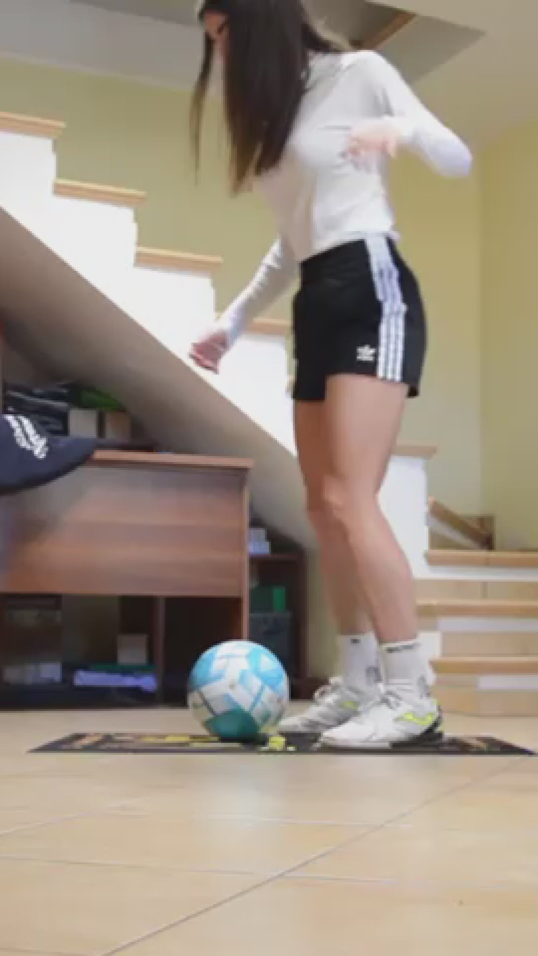 Soccer player practicing ball control on a training mat in an indoor space, wearing sporty attire.